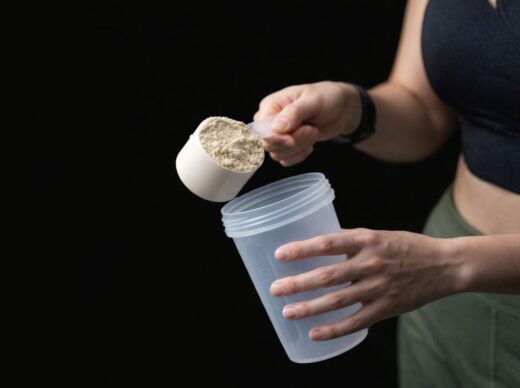 En person häller en skopa proteinpulver i en shakerflaska för träning.