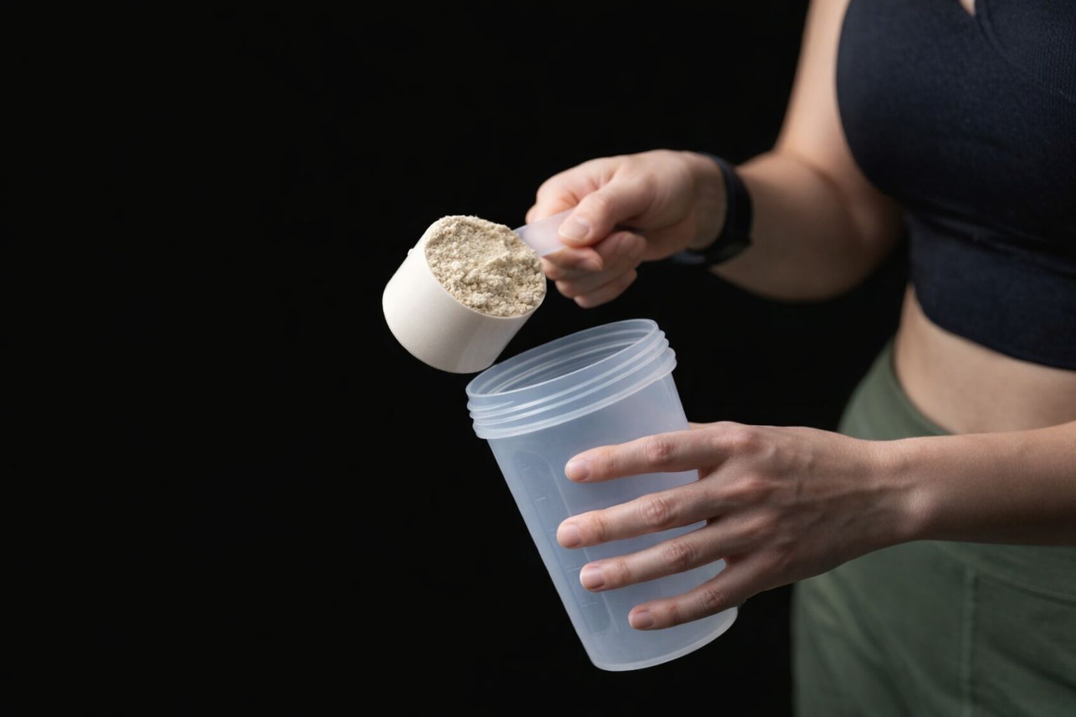 En person häller en skopa proteinpulver i en shakerflaska för träning.