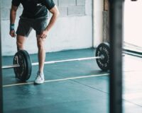 Person i träningsskor står framför en skivstång med vikter i gymmet