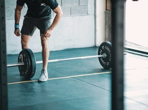 Person i träningsskor står framför en skivstång med vikter i gymmet