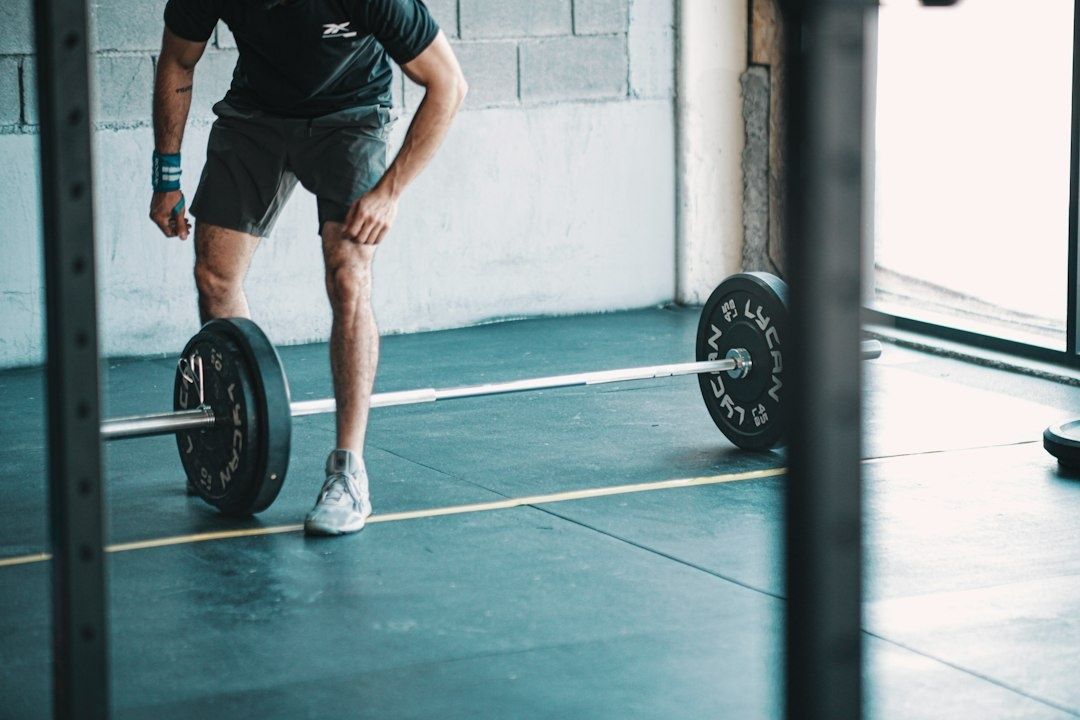 Person i träningsskor står framför en skivstång med vikter i gymmet