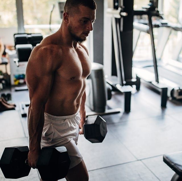 Barbröstad man bär tunga hantlar i ett gym